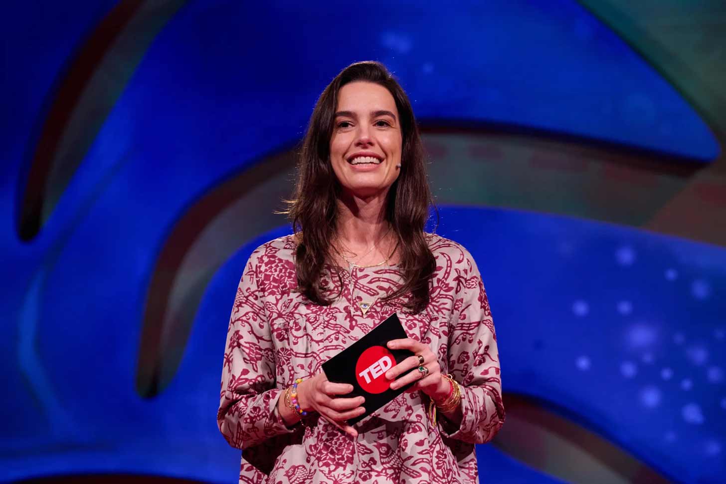A woman, Logan McClure Davda, stands on stage at TED