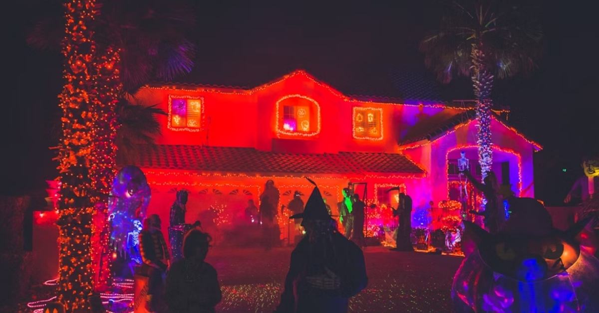 A house lit up red for Halloween with a crowd of costumed partygoers milling out on a lawn at night. 