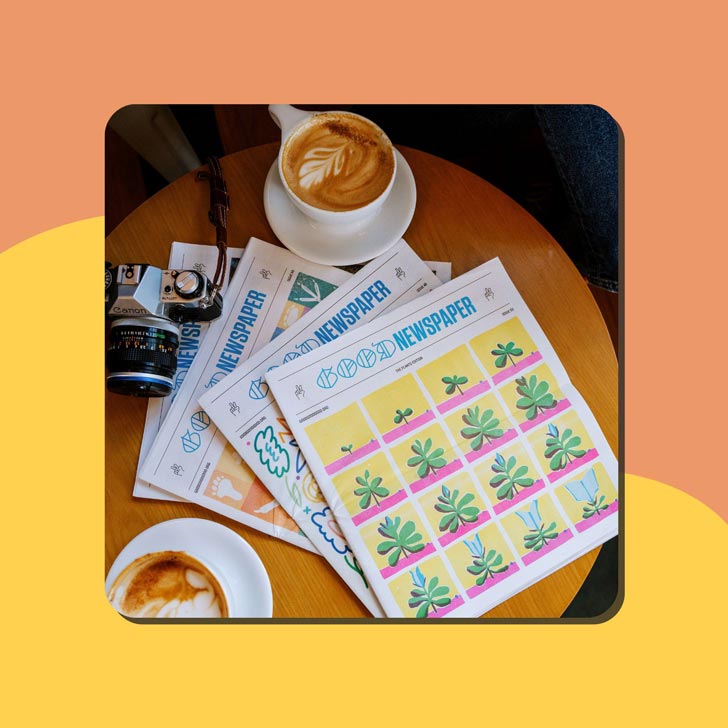 Four Goodnewspapers sit on a table next to a mug of coffee