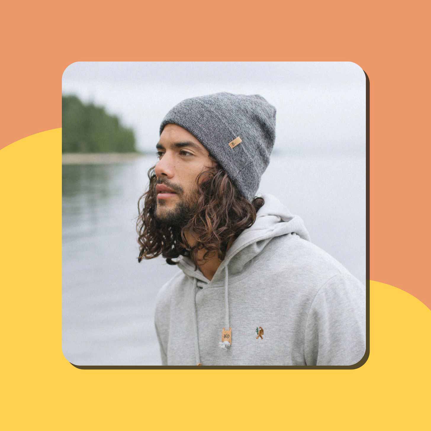 A man with long brown curly hair wears a grey beanie from Tentree