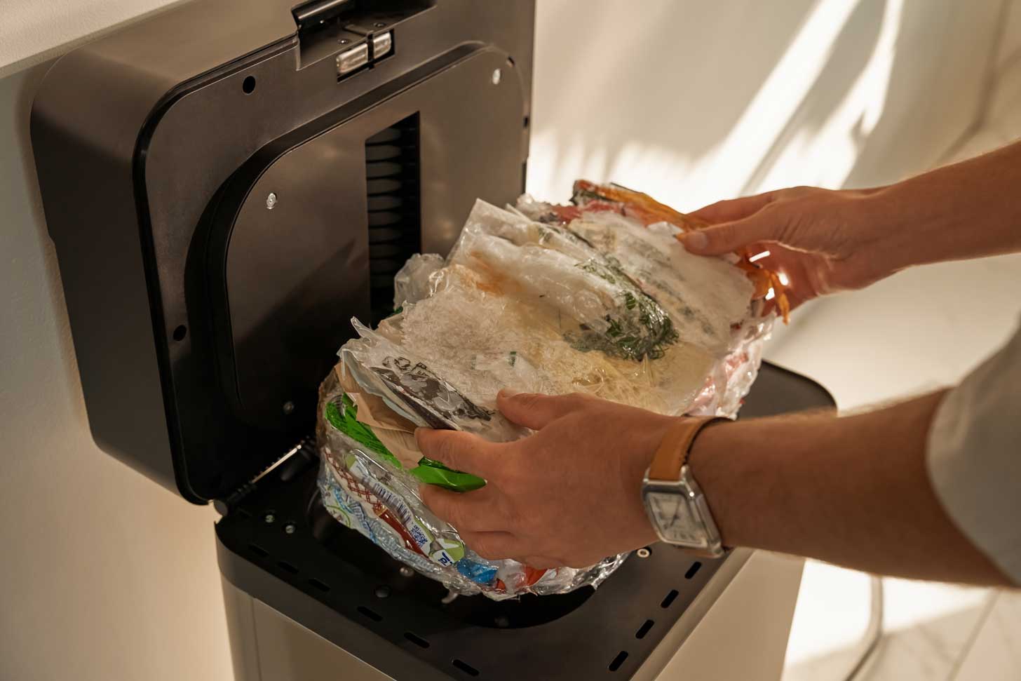 A person picks up a block of condensed recycled plastics from a garbage bin