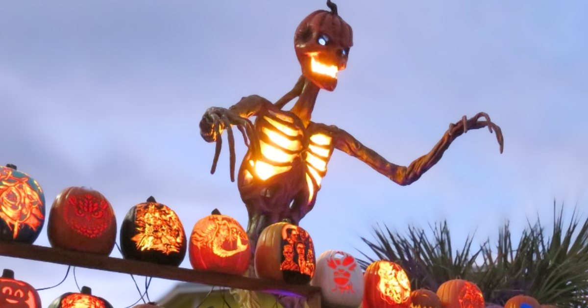 A tall skeleton decoration glowing orange as it lords over jack-o-lanterns