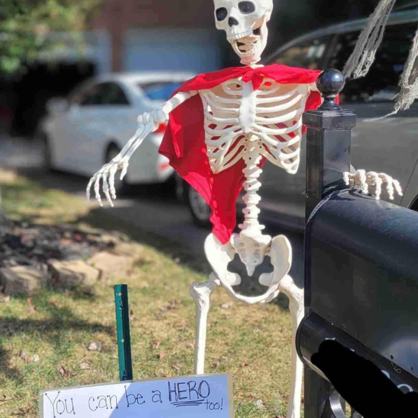 A skeleton wearing a cape holds out a sign that says "You can be a hero too!"