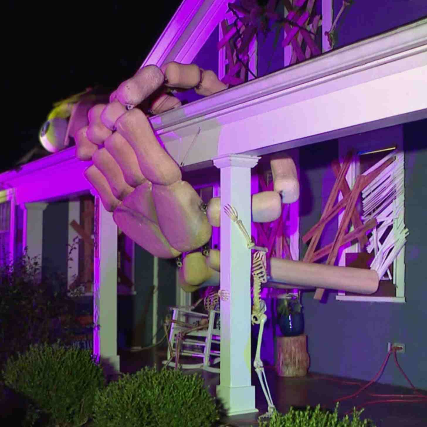A giant skeleton hand reaches through a doorway and hangs on to the roof of the house