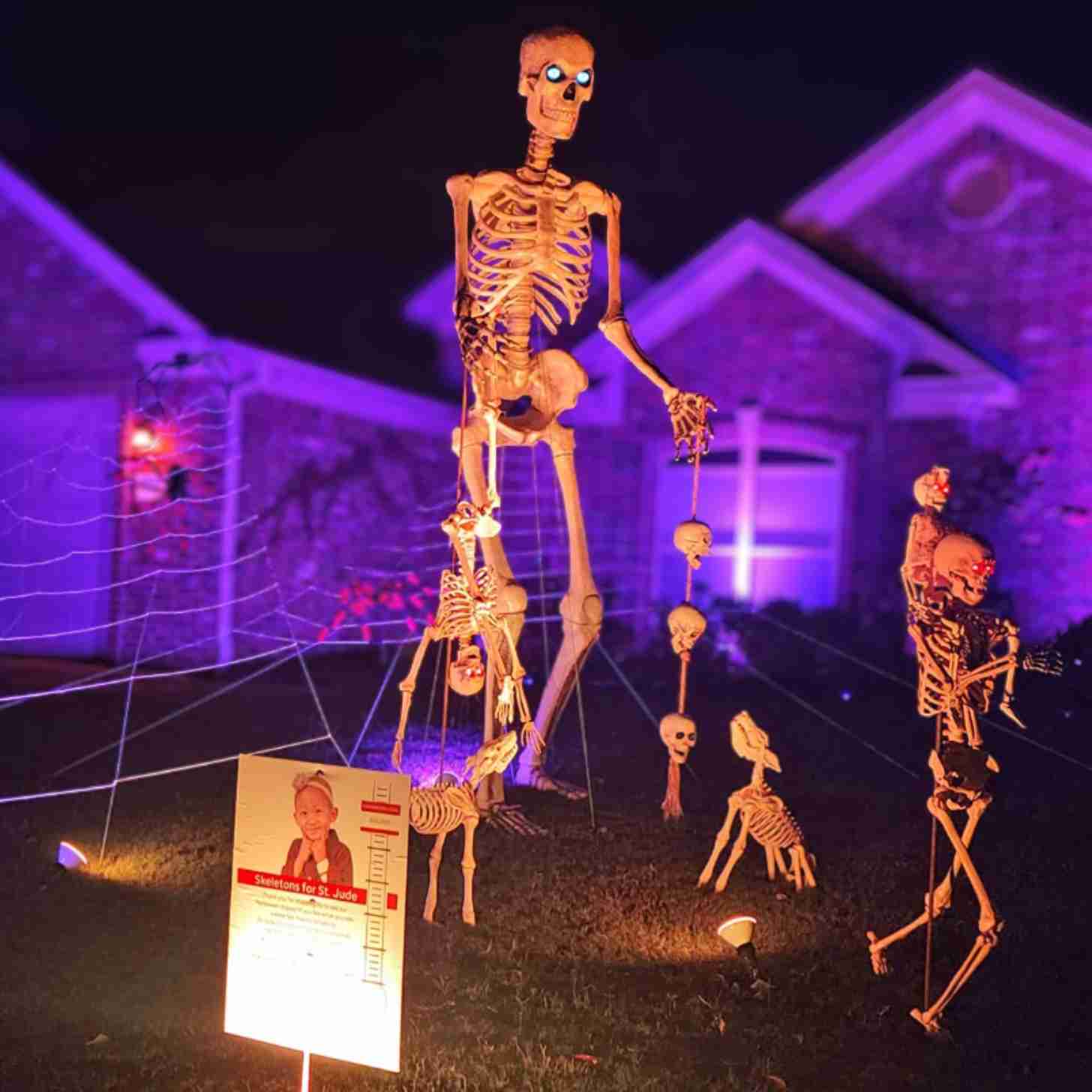 A tall skeleton surrounded by baby skeletons in the middle of a yard Halloween display lit up at night