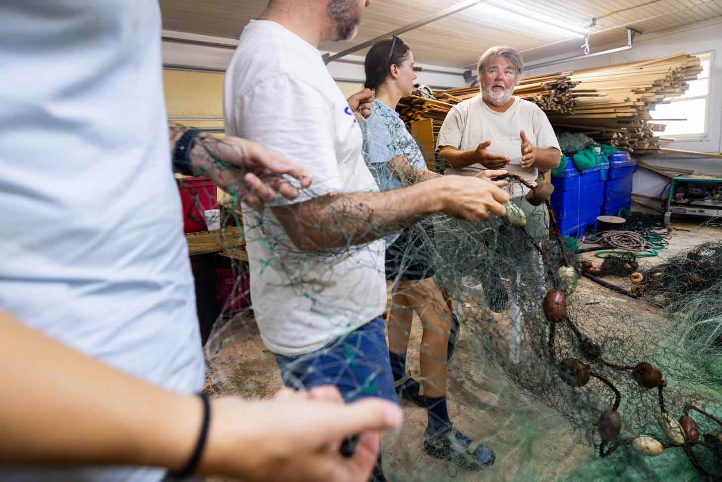A man with gray hair and a beard speaks to a group of researchers, all holding a fishing net