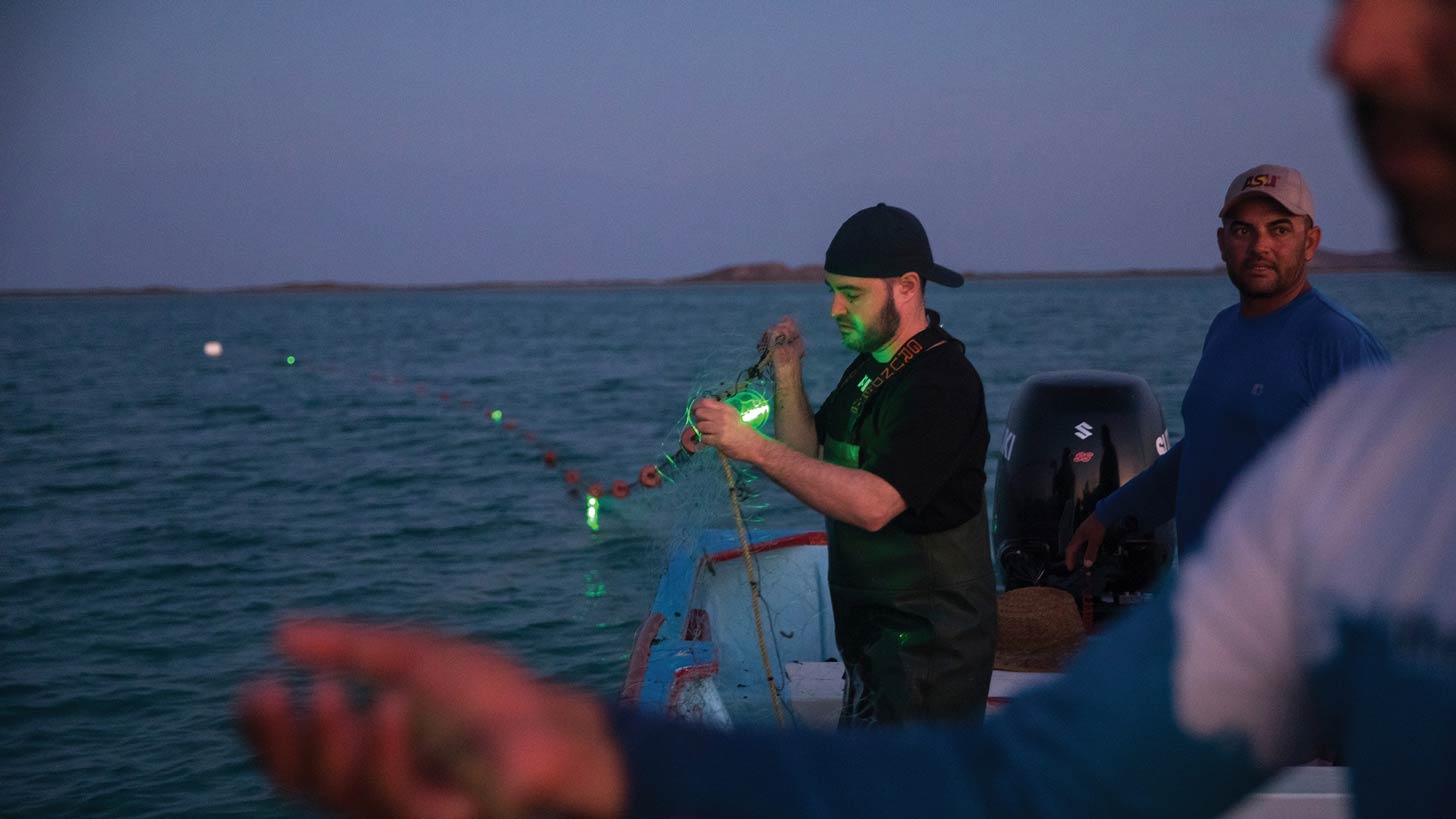 A man strings green LED lights to fishing nets in the water