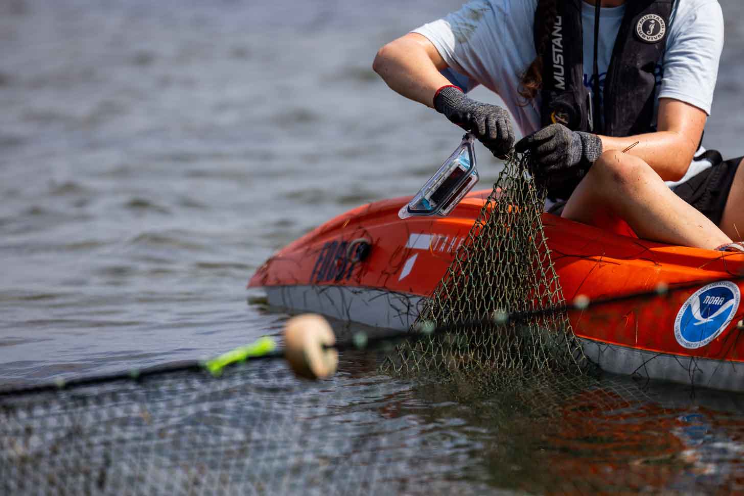 A close-up of a person attaching an LED light to a green fishing net from an orange kayak