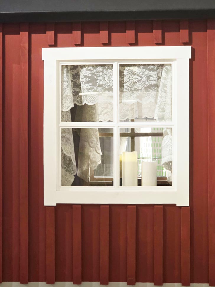 A close-up of a white window with lace curtains on a red home