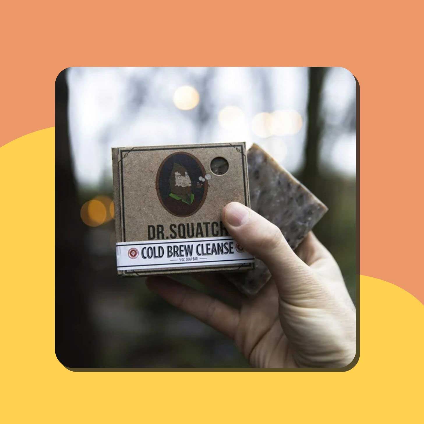 A hand holds up a bar of Dr. Squatch soap