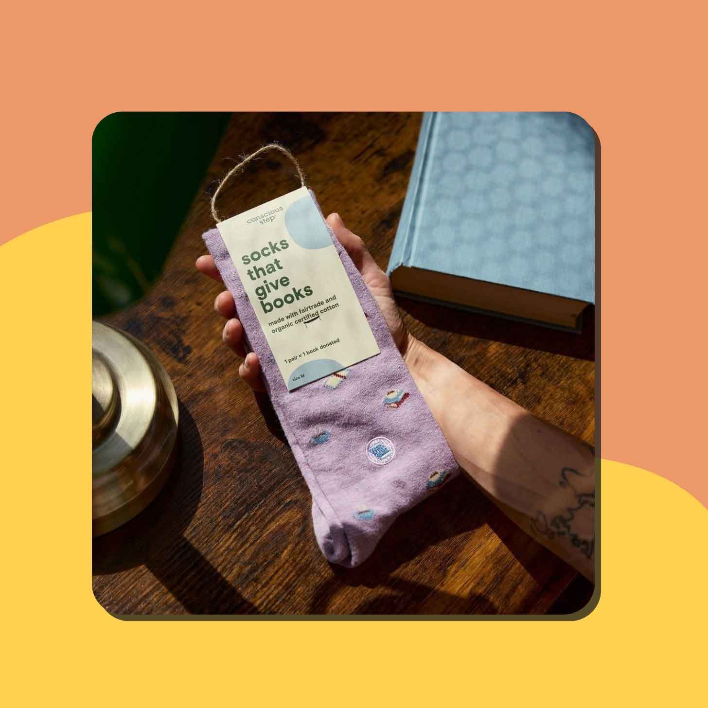 A hand holds up a pair of purple Conscious Step socks