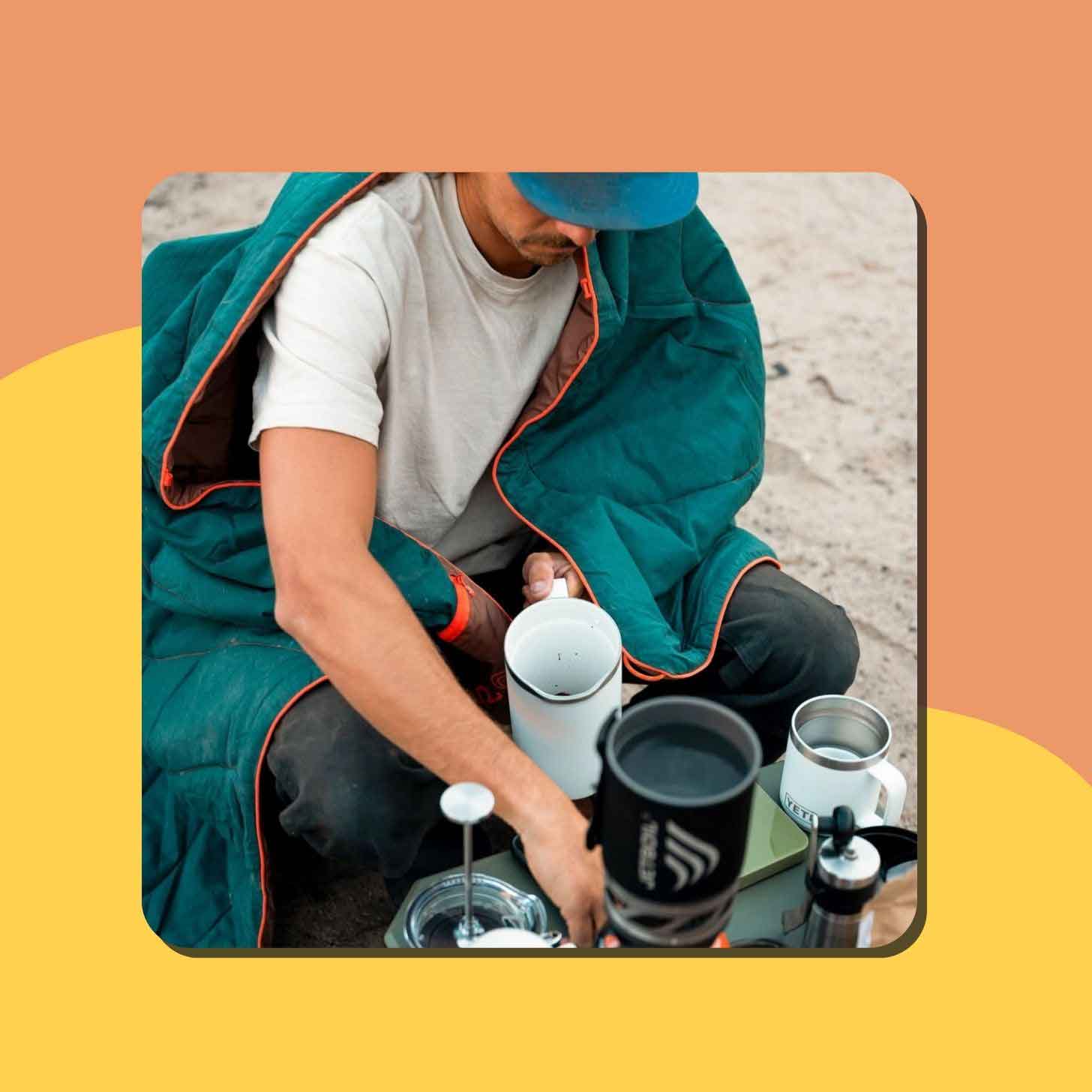 A person sits on a beach, wrapped in a teal Rumpl blanket