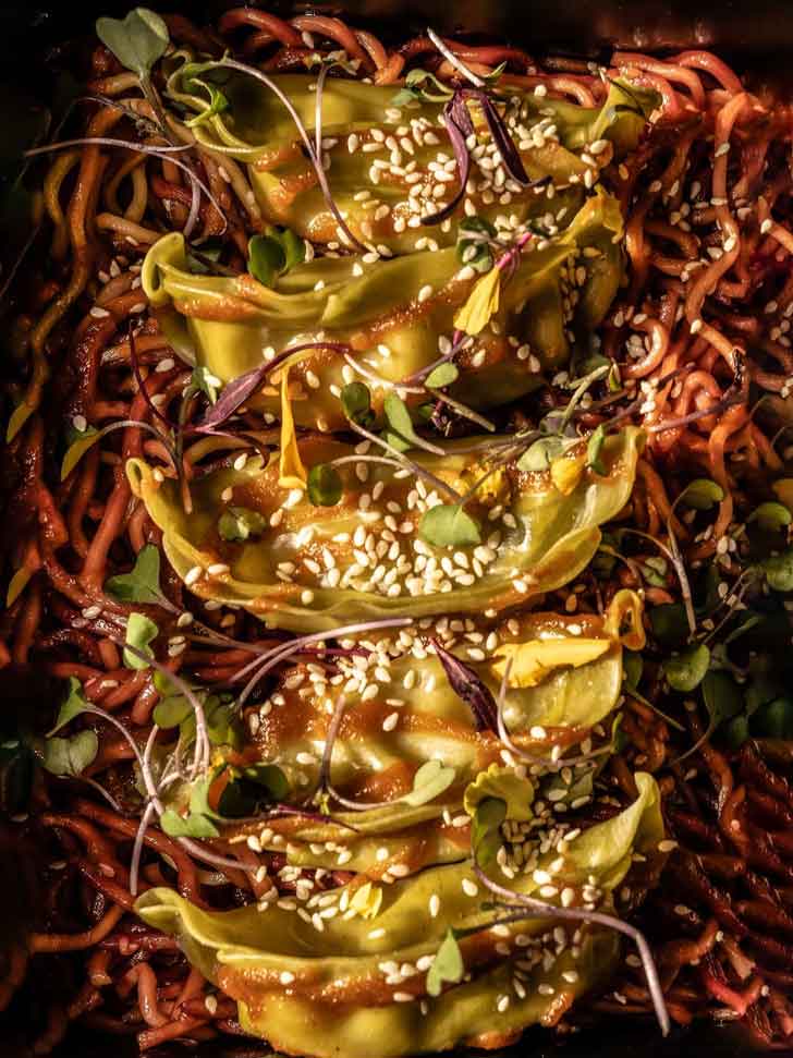 Steamed dumplings atop a bed of noodles, covered in sprouts and sesame seeds