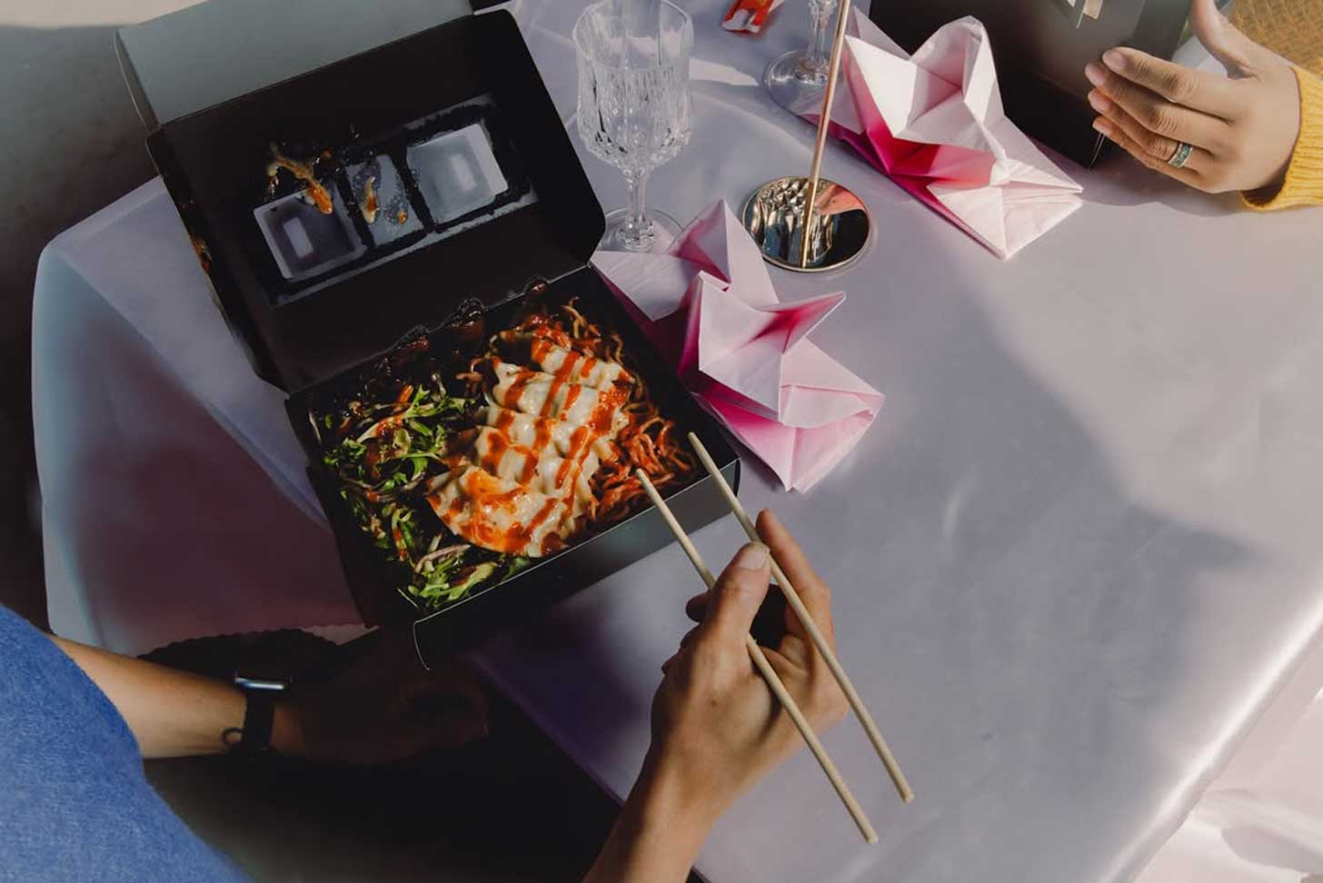 Two people eat dumplings out of takeout containers at a table