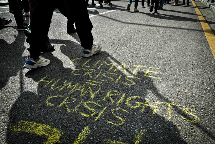 Yellow chalk writing on asphalt reads: "Climate crisis = human rights crisis"
