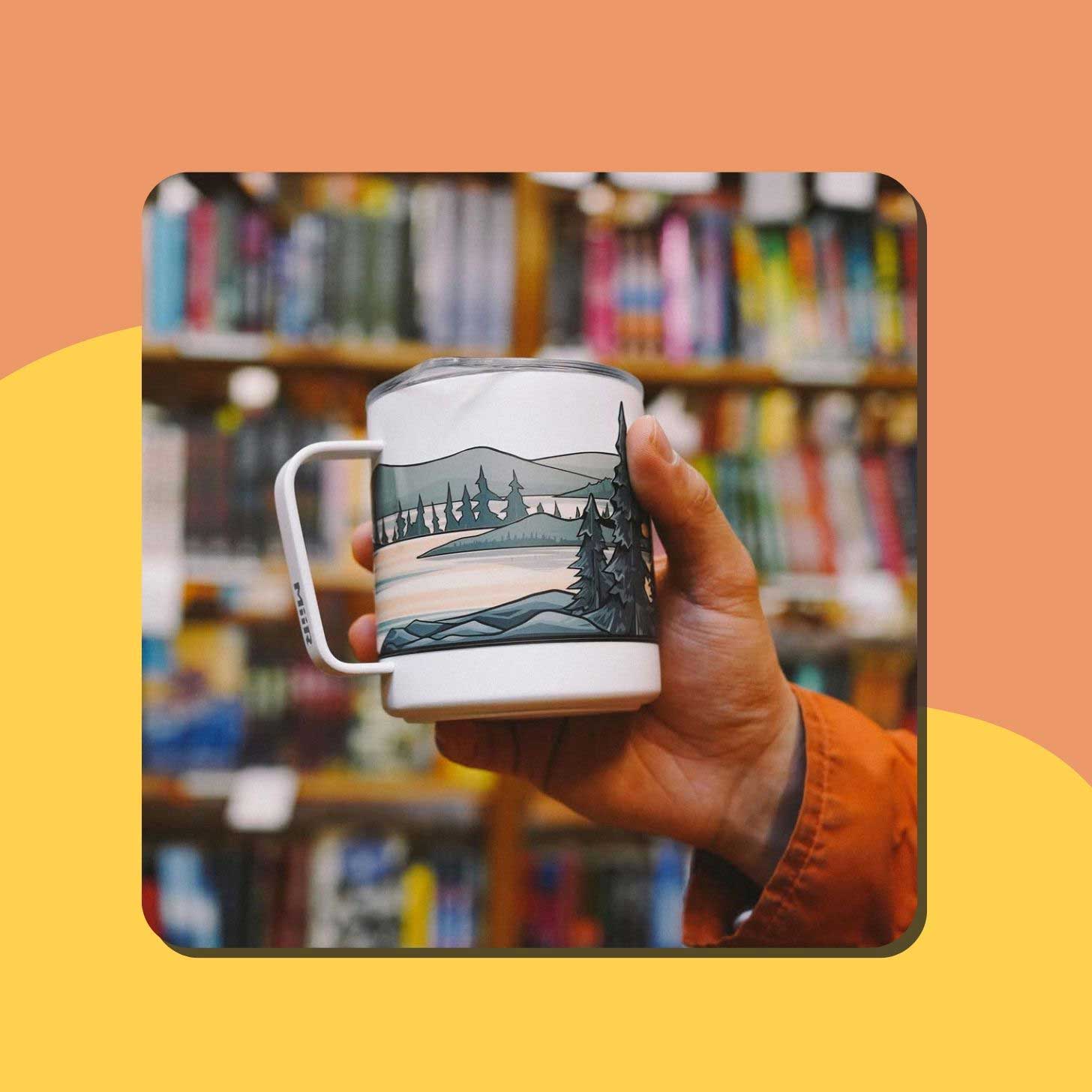 A person holds up a mug with a landscape sticker on it