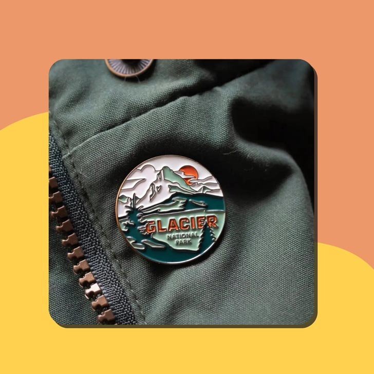 An enamel pin that reads "Glacier National Park"