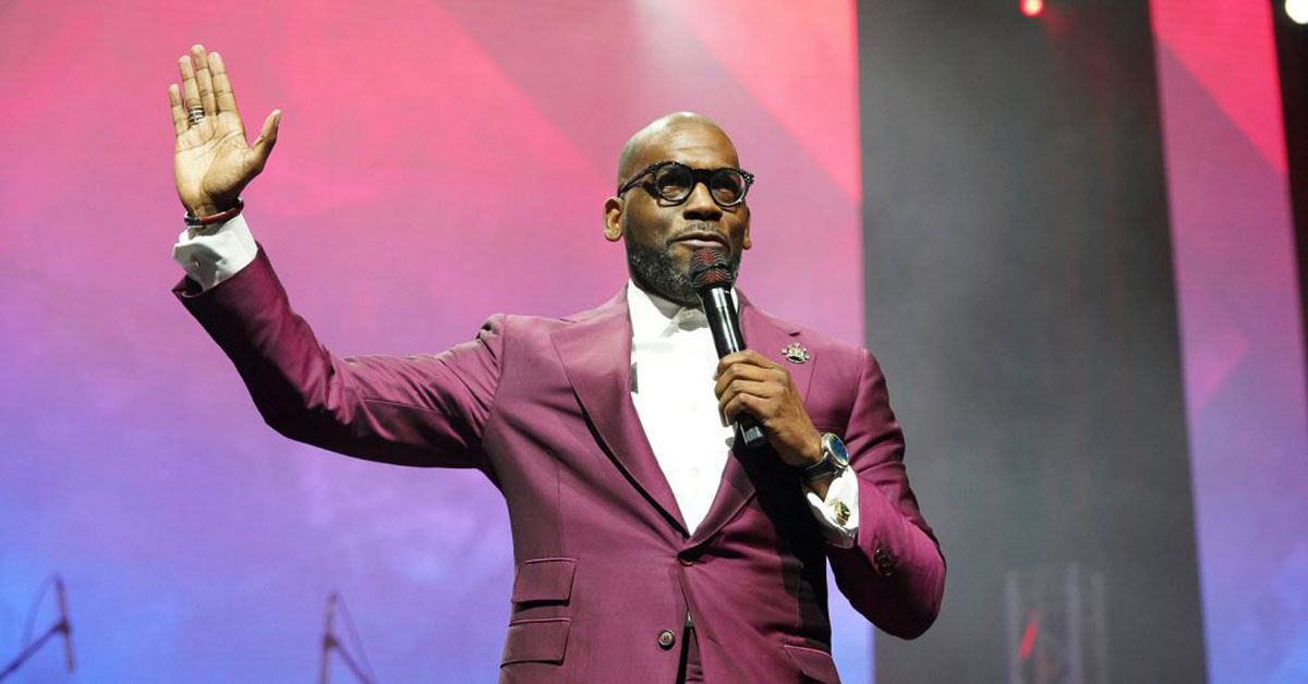 Pastor Jamal H. Bryant raises his hand in worship while speaking into a microphone on stage