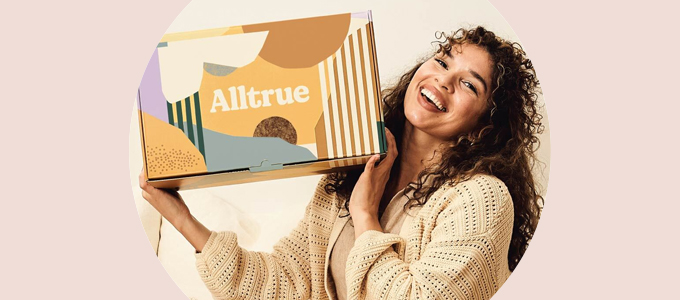 A woman smiles and holds an Alltrue subscription box up.