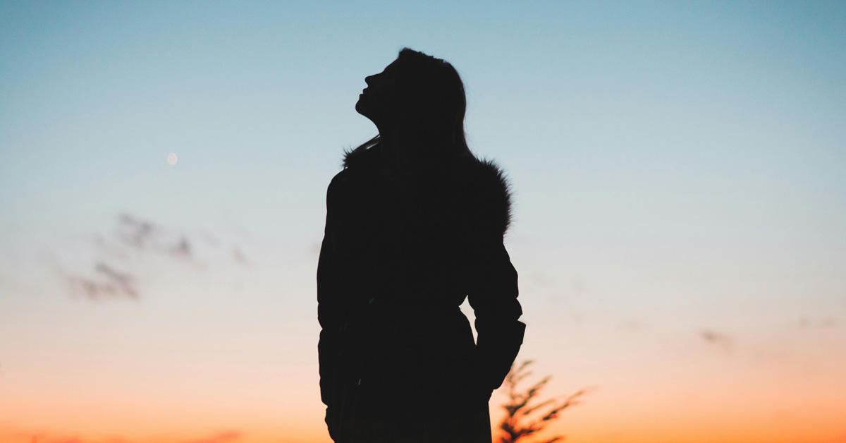 A silhouette of a woman looking up at a sunset
