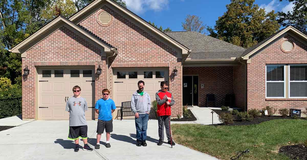 Four young men with disabilities stand in front of a house