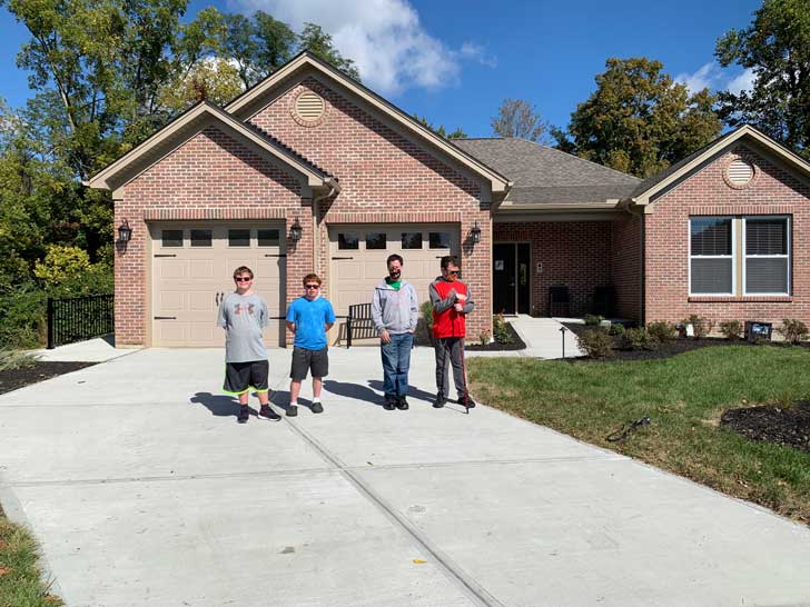 Four young men with disabilities stand in front of a house