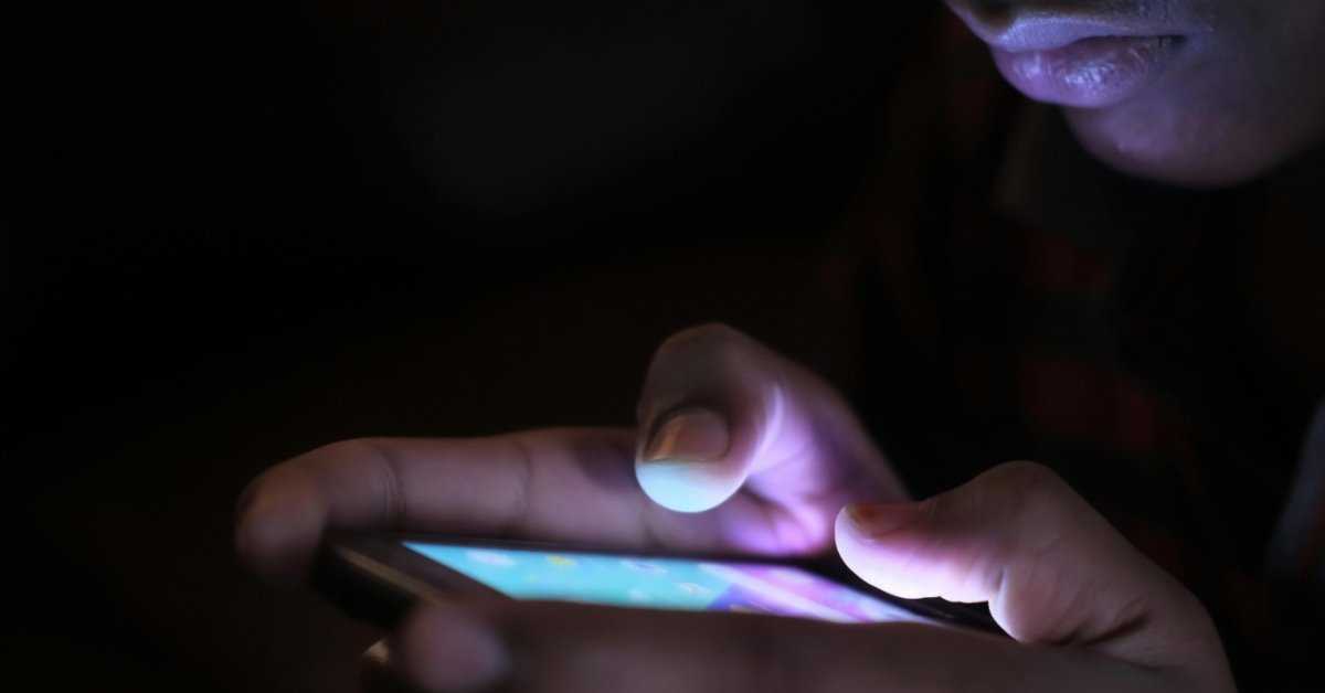 A woman looks at her glowing iPhone screen in a dark room