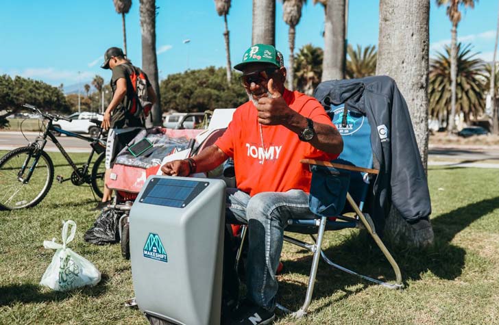 A man experiencing homelessness in California gives a thumbs-up while holding his Makeshift Traveler backpack