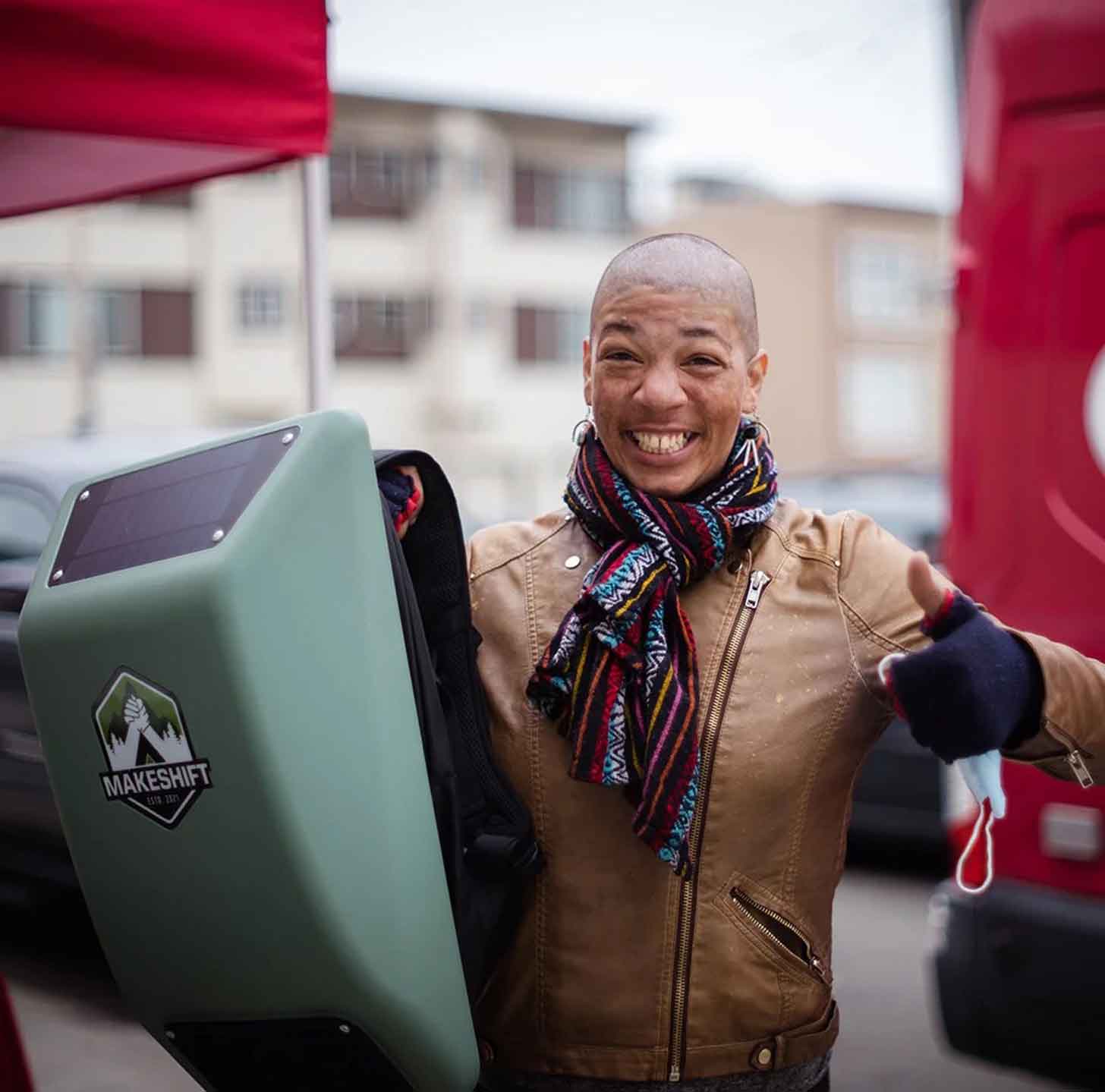 A person holds up a Makeshift Traveler backpack, giving a thumbs-up and smiling