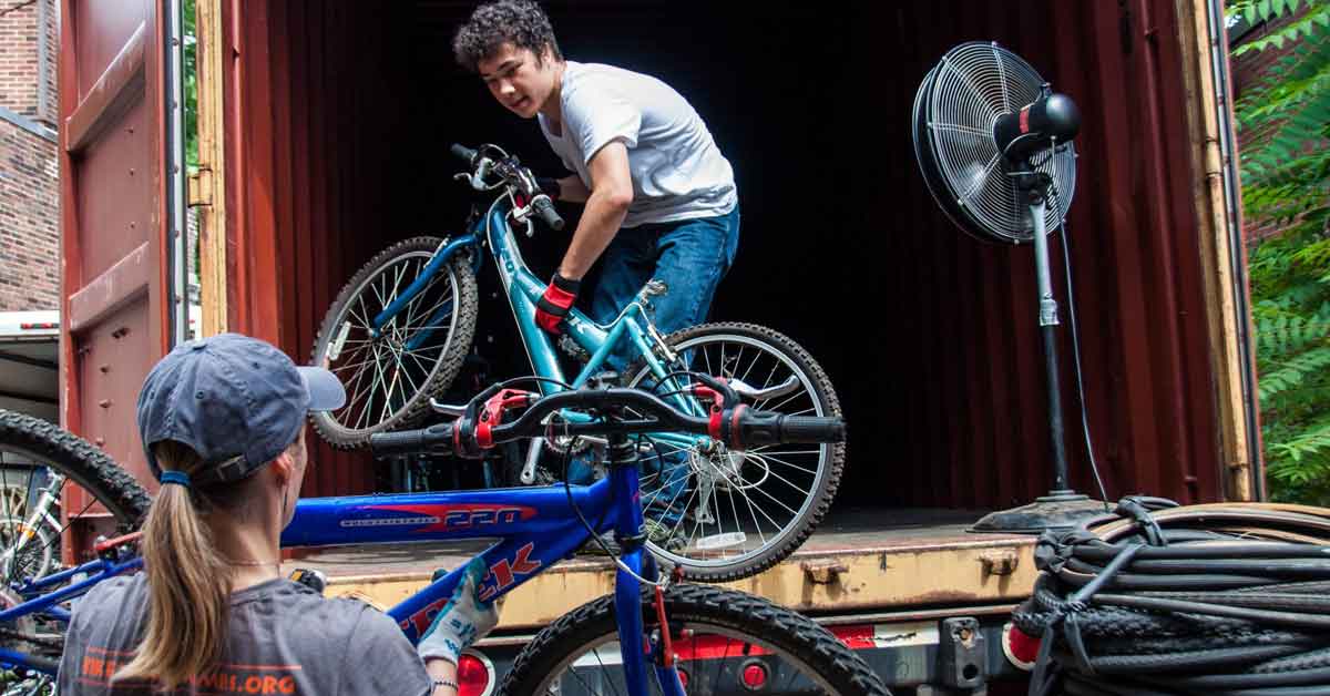 A young man takes a bike out of a shipping container and hands it to another person