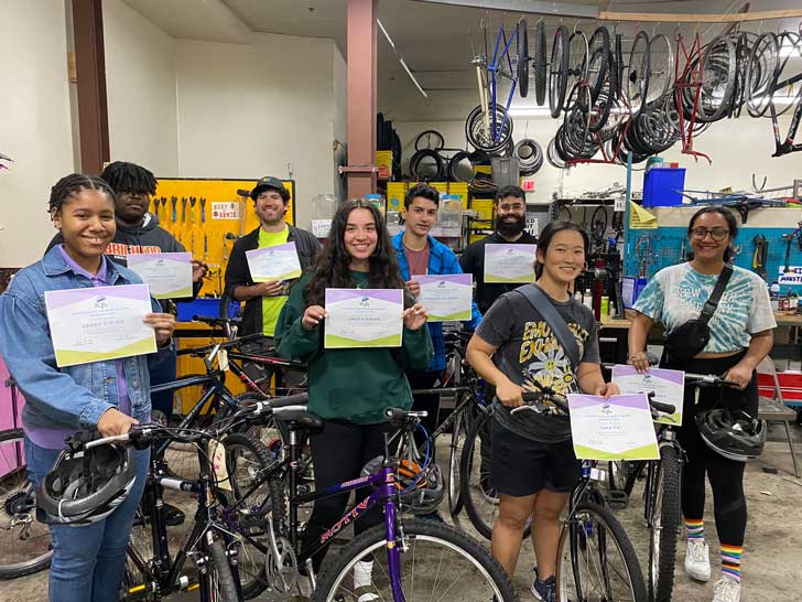 A group of teenagers holds certificates next to bicycles in a bike shop in Boston