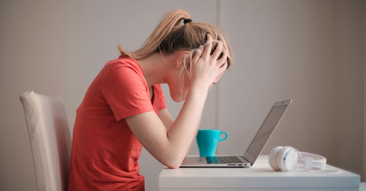 A young woman sits hunched over a laptop, head in her hands