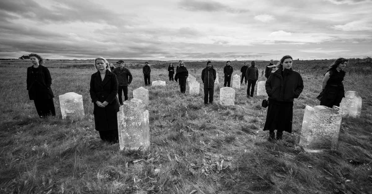 People stand, wearing all black, near grave stones made from ice