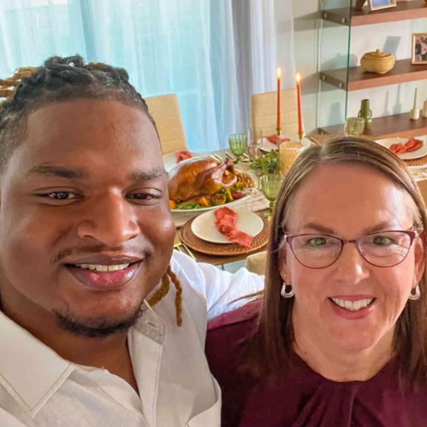 Jamal, a Black man, and Wanda, a white woman, smile together with thanksgiving food behind them
