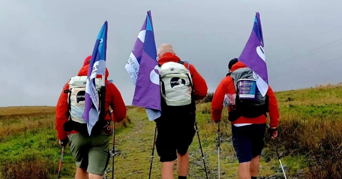 Three dads walk on a foggy trail as they carry suicide awareness flags in their backpacks
