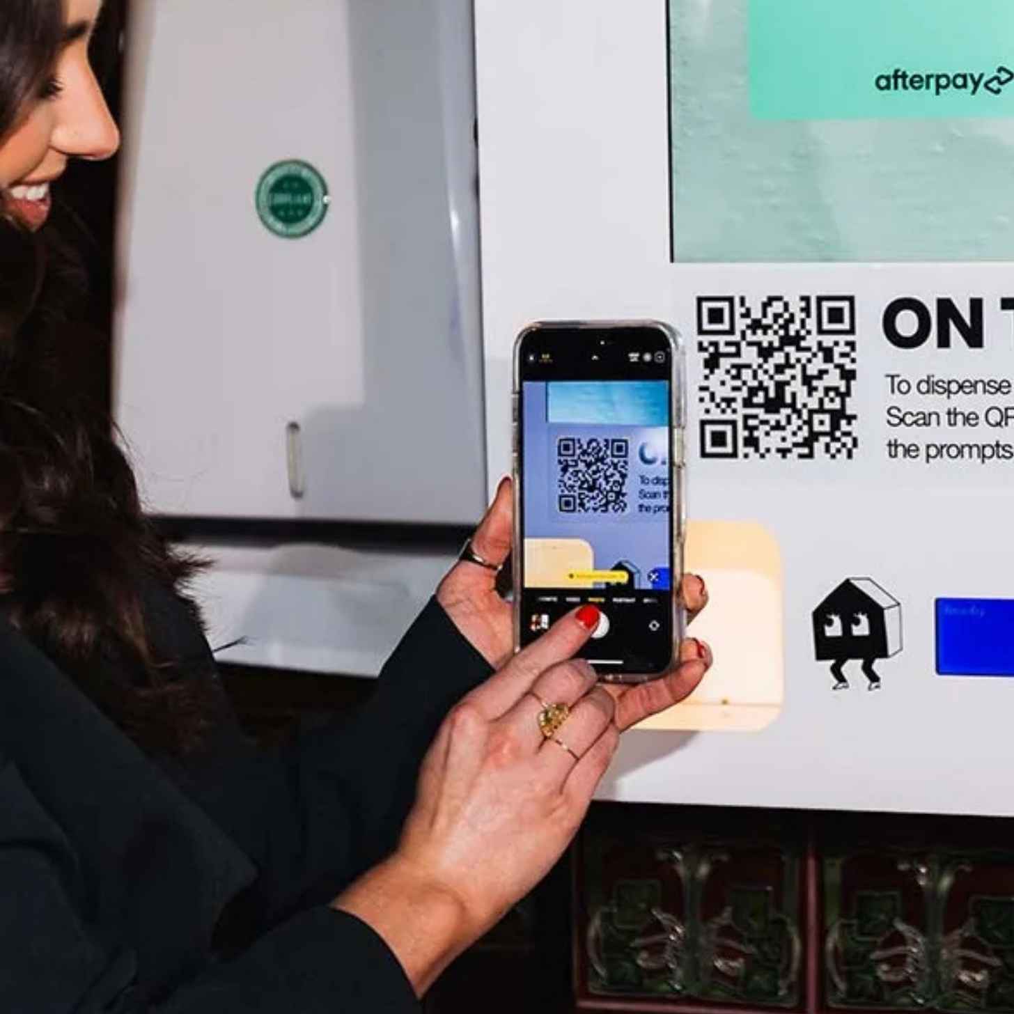 A smiling woman scans a QR code on a digital billboard