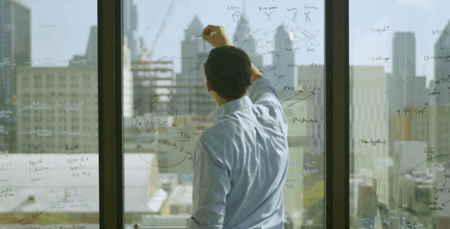 Dr. David Fajgenbaum writes in marker on a window