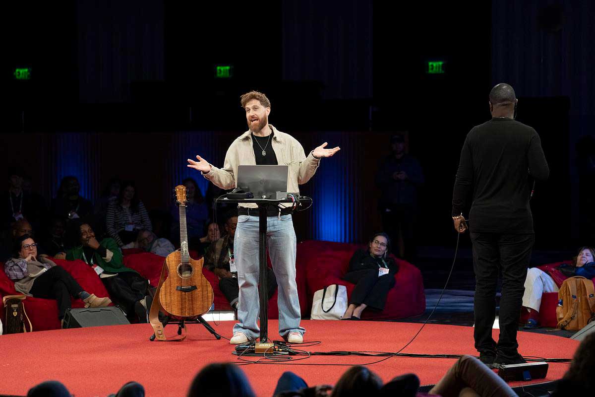 A man shrugs with his arms open behind a laptop 