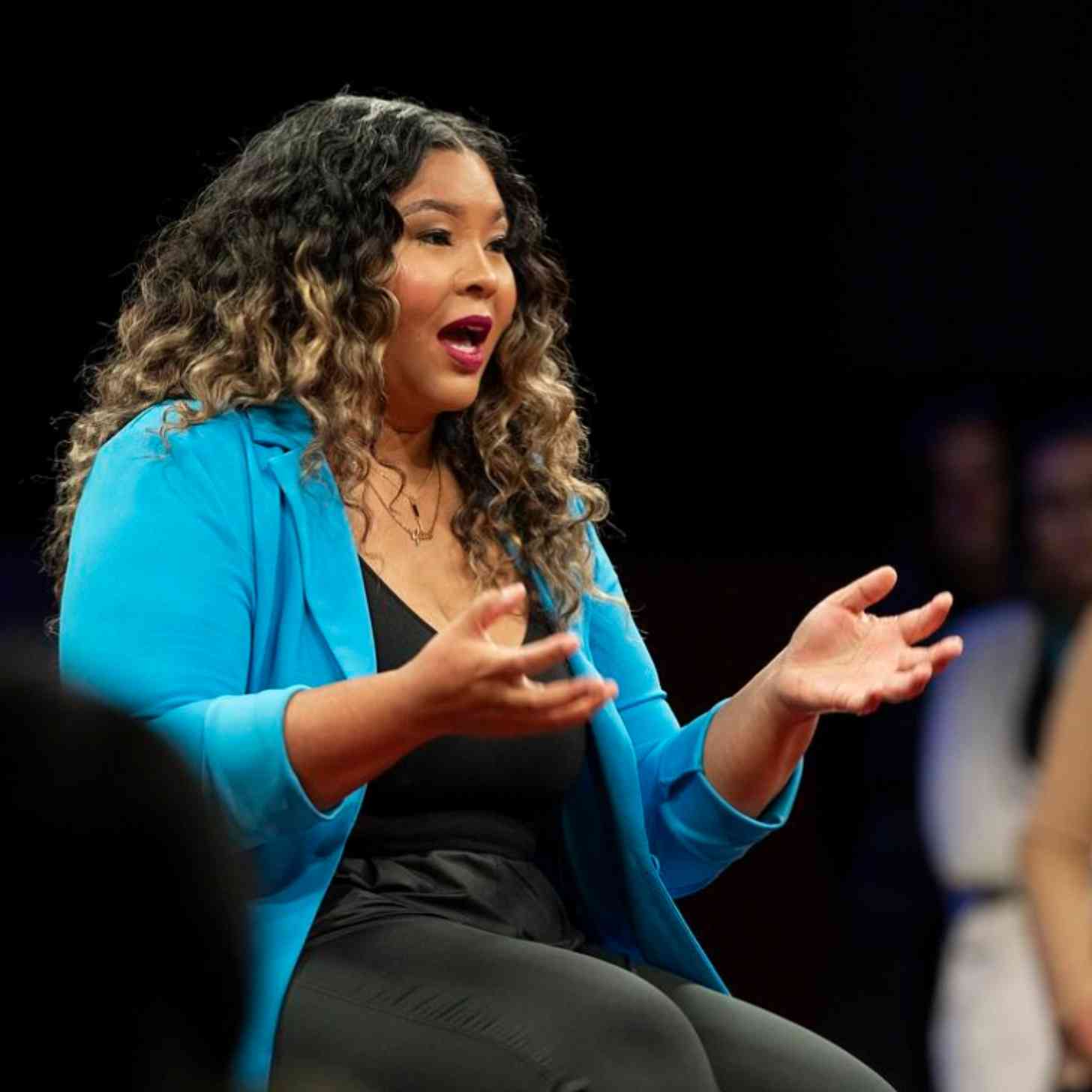 A woman in blue blazer speaks on a conference stage