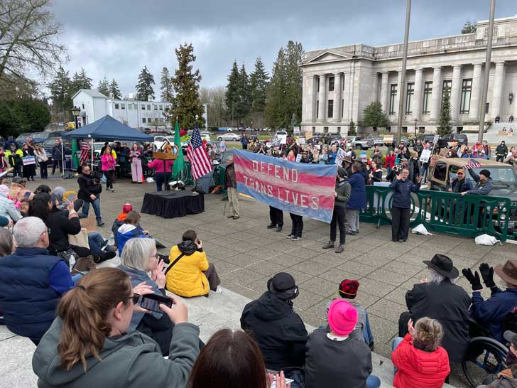 Protestors hold up a large banner that reads "Defend trans lives."