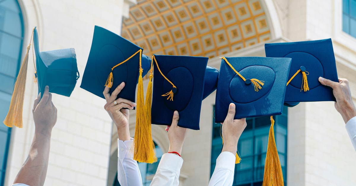 A close-up of people holding graduation caps in the air
