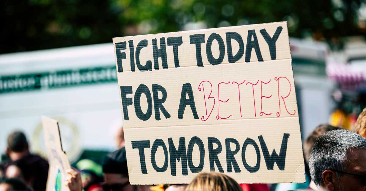 A cardboard protest sign reads: "Fight today for a better tomorrow."