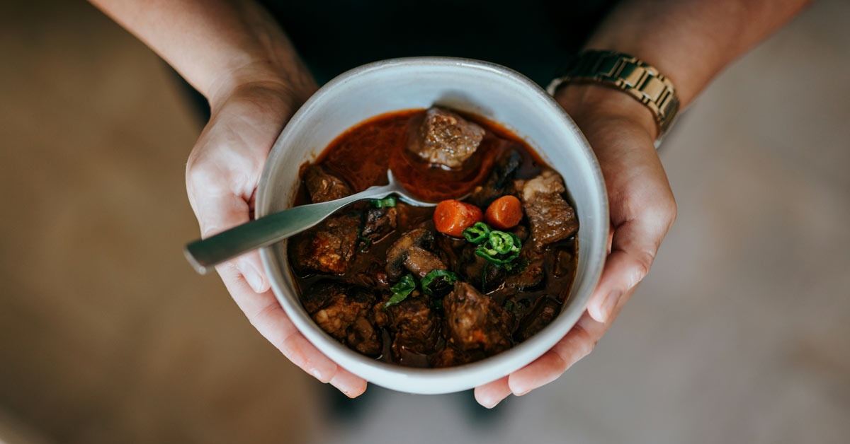 A person holds a bowl of stew in a white ceramic bowl