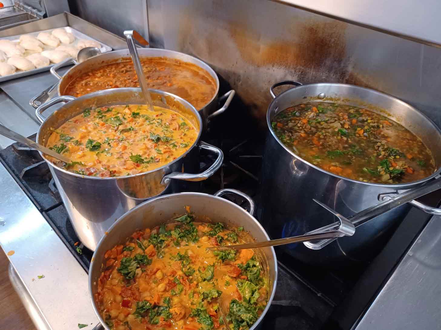 Three large pots of soup sit on a stove