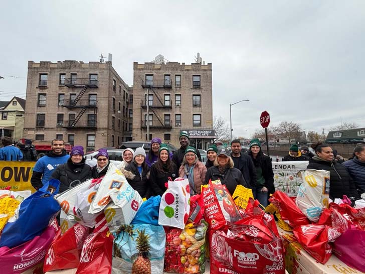 A large group photo of Alexandria Ocasio-Cortez and about a dozen volunteers, all smiling with a slew of reusable grocery bags