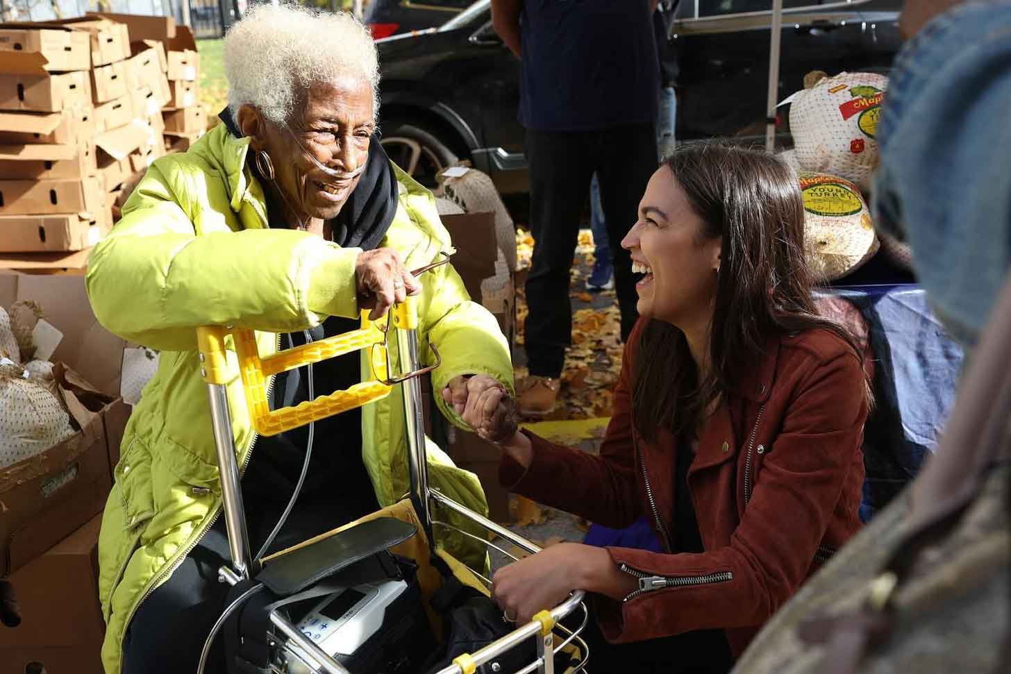 Congresswoman Alexandria Ocasio-Cortez kneels to meet a constituent in a wheelchair during a Thanksgiving turkey distribution