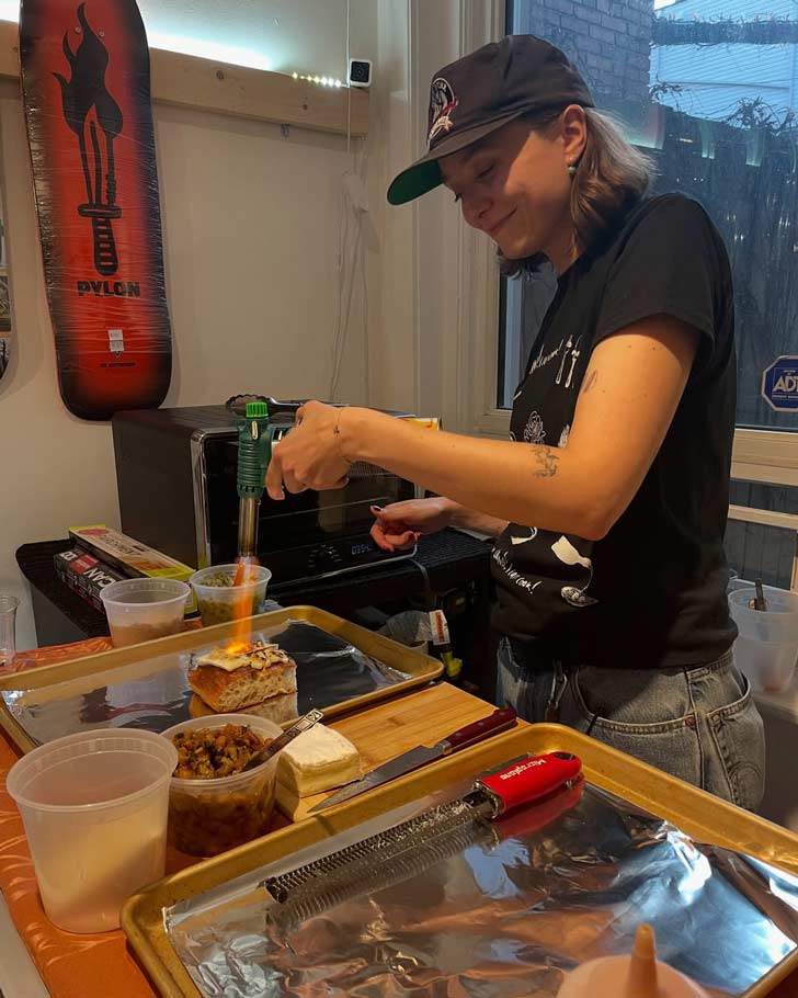A young woman uses a torch to cook a meal in a makeshift kitchen