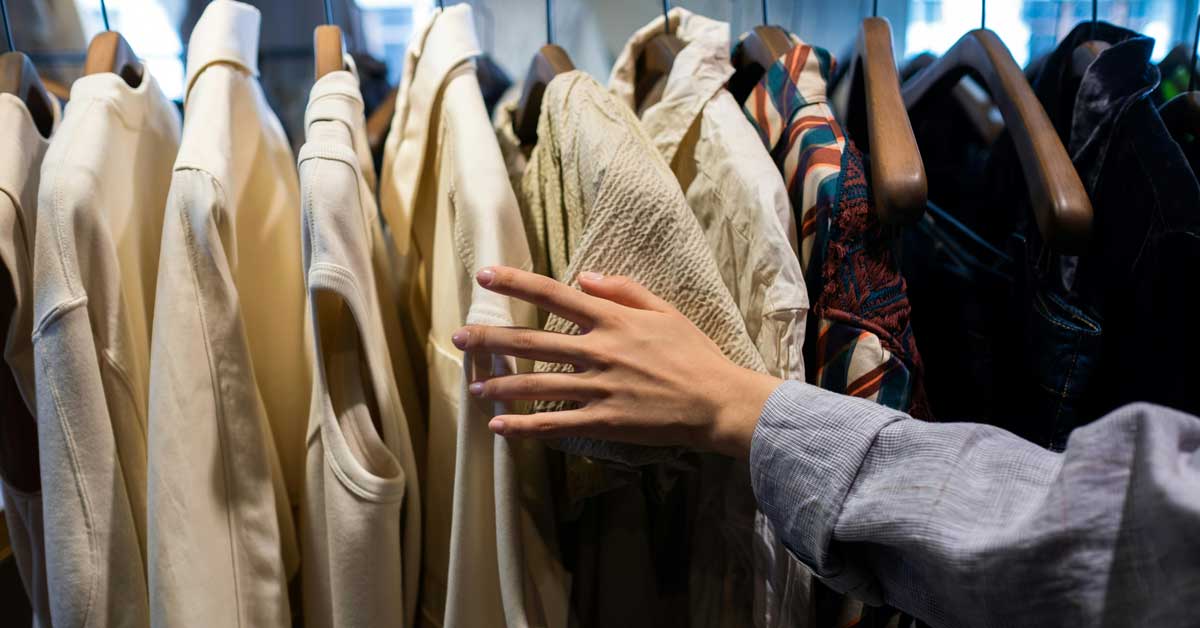 A woman's hand reaches for an article of clothing off of a rack full of shirts on hangers