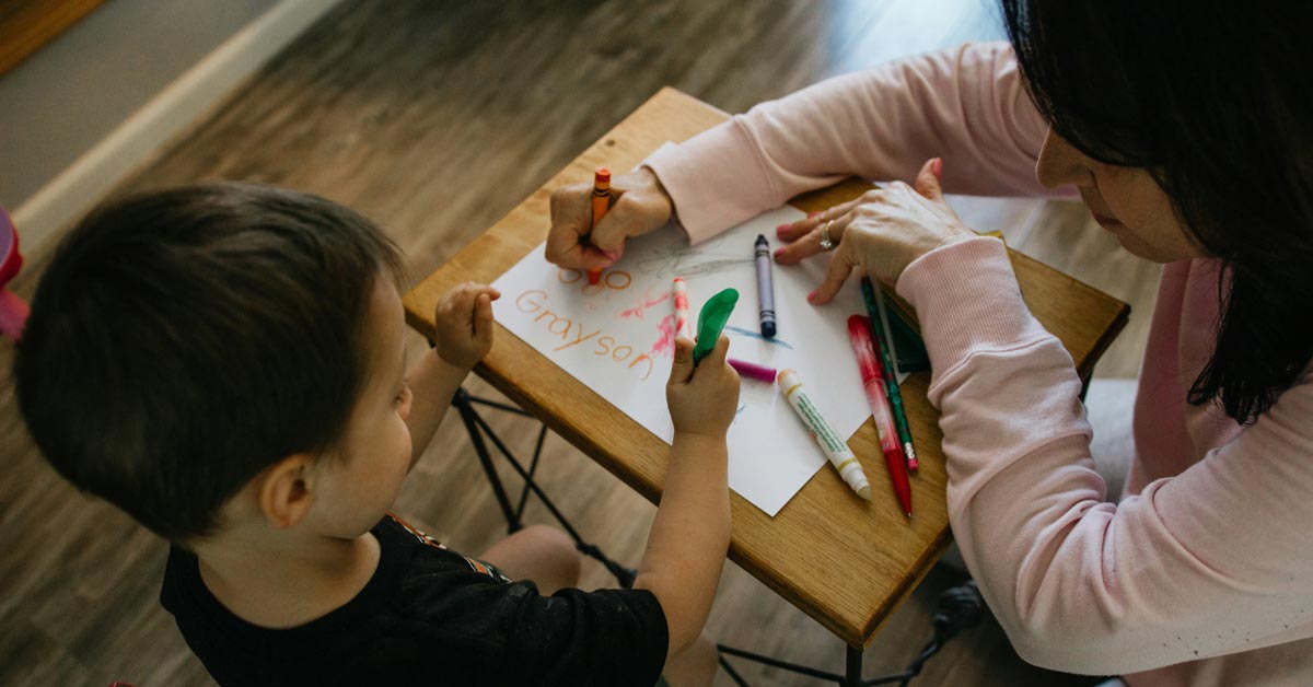 A woman and a young boy color on a piece of paper with crayons