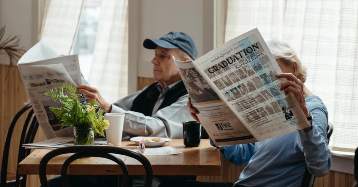 Two seniors read The Midcoast Villager side by side as they sit inside the Villager Cafe 